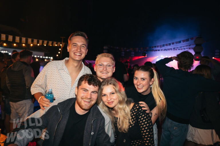 Beim Wild Woods Festival feiern Gäste in der Nacht vor der Bühne, umgeben von blauem und buntem Licht, mit Lächeln und guter Stimmung.
