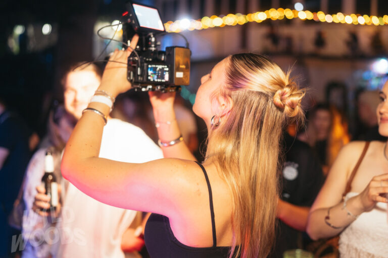 Impressionen von Wild Woods: eine Person mit blonden Haaren am DJ-Pult, umgeben von warmen goldenen Lichtern und Technik im Nachtlicht.