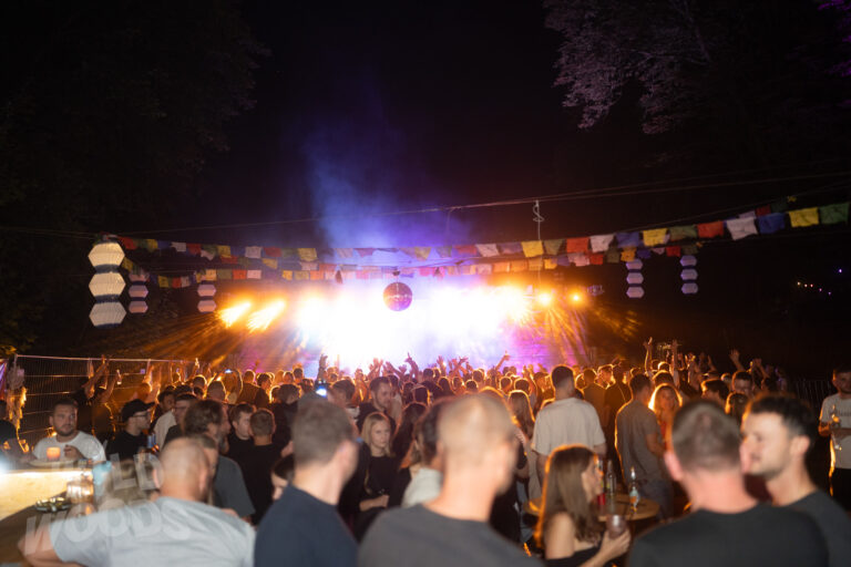 Beim Wild Woods Festival im Märchenwald tanzt das Publikum vor der Bühne mit lila-orangen Lichtstrahlen, Nebel, Discokugel unter bunten Girlanden.