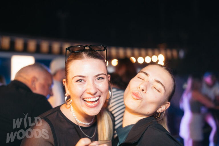 Fröhliche Besucherinnen beim Wild Woods Festival im Märchenwald, Nachtlicht und Lichterscheinung im Hintergrund, Close-up im Partybereich