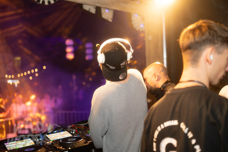 Wild Woods Festival im Märchenwald: DJ am Mischpult mit weißen Kopfhörern, goldenem Licht und lila Scheinwerfern auf der Bühne.