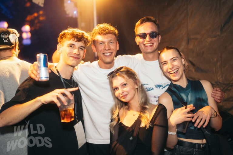 Wild Woods: Gruppe junger Leute mit warmem Licht, Sonnenbrille und weißen Shirts, Drinks in der Hand, fröhliche Stimmung bei Elektronische Musik